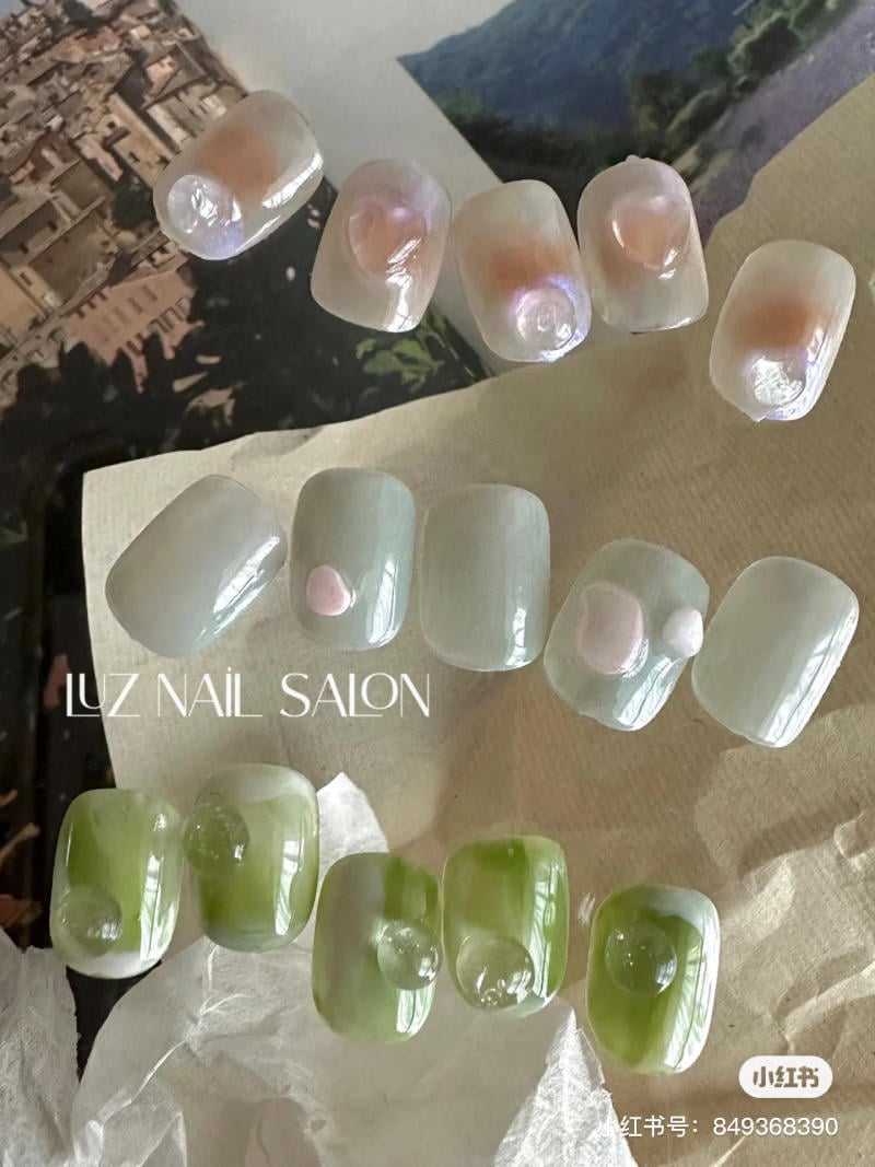 Bộ m&oacute;ng giả với thiết kế đa dạng m&agrave;u sắc, gồm m&agrave;u pastel v&agrave; xanh l&aacute;, đặt tr&ecirc;n bề mặt giấy.