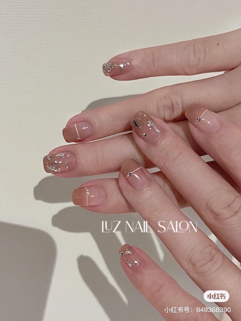 B&agrave;n tay với m&oacute;ng tay được sơn m&agrave;u nude nhạt, trang tr&iacute; họa tiết bạc lấp l&aacute;nh, nền trắng.