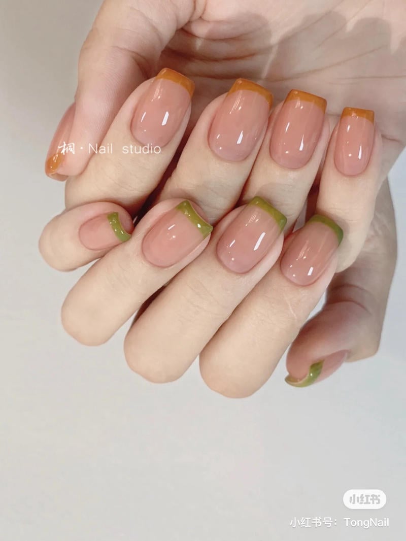 B&agrave;n tay với m&oacute;ng tay sơn kiểu Ph&aacute;p, đầu m&oacute;ng m&agrave;u cam v&agrave; xanh l&aacute;, nền m&agrave;u nude.