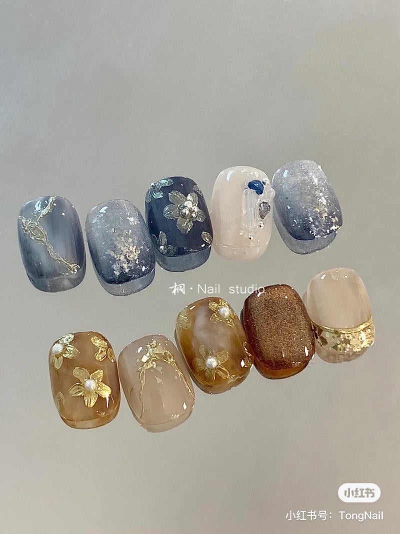 Bộ m&oacute;ng tay giả với hoa văn v&agrave; m&agrave;u sắc đa dạng, bao gồm xanh, n&acirc;u v&agrave; hoa trang tr&iacute;.