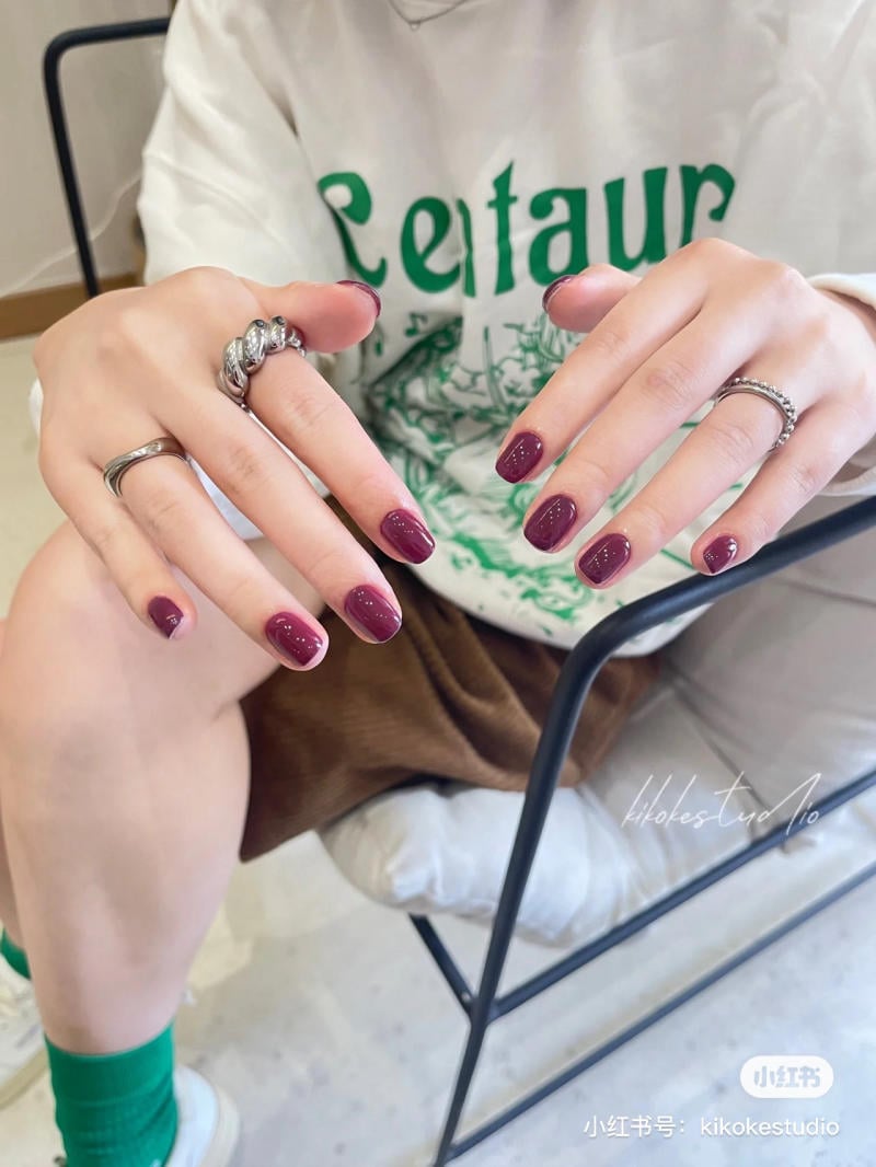 Người ngồi tr&ecirc;n ghế, tay sơn m&oacute;ng m&agrave;u đỏ t&iacute;a, đeo nhẫn bạc, mặc &aacute;o thun trắng in chữ xanh.