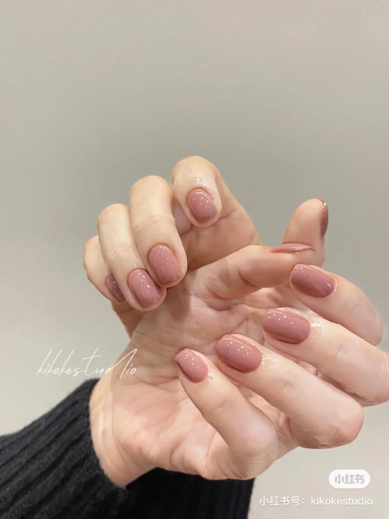 B&agrave;n tay với m&oacute;ng tay được sơn m&agrave;u hồng nhạt, nền x&aacute;m, &aacute;o len đen.