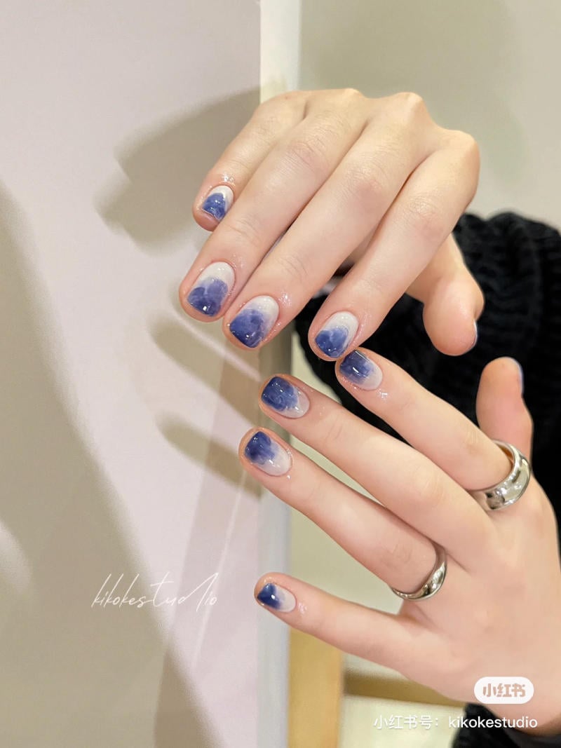 B&agrave;n tay đeo nhẫn với m&oacute;ng tay được sơn m&agrave;u xanh đậm nhạt, nổi bật tr&ecirc;n nền &aacute;o đen.