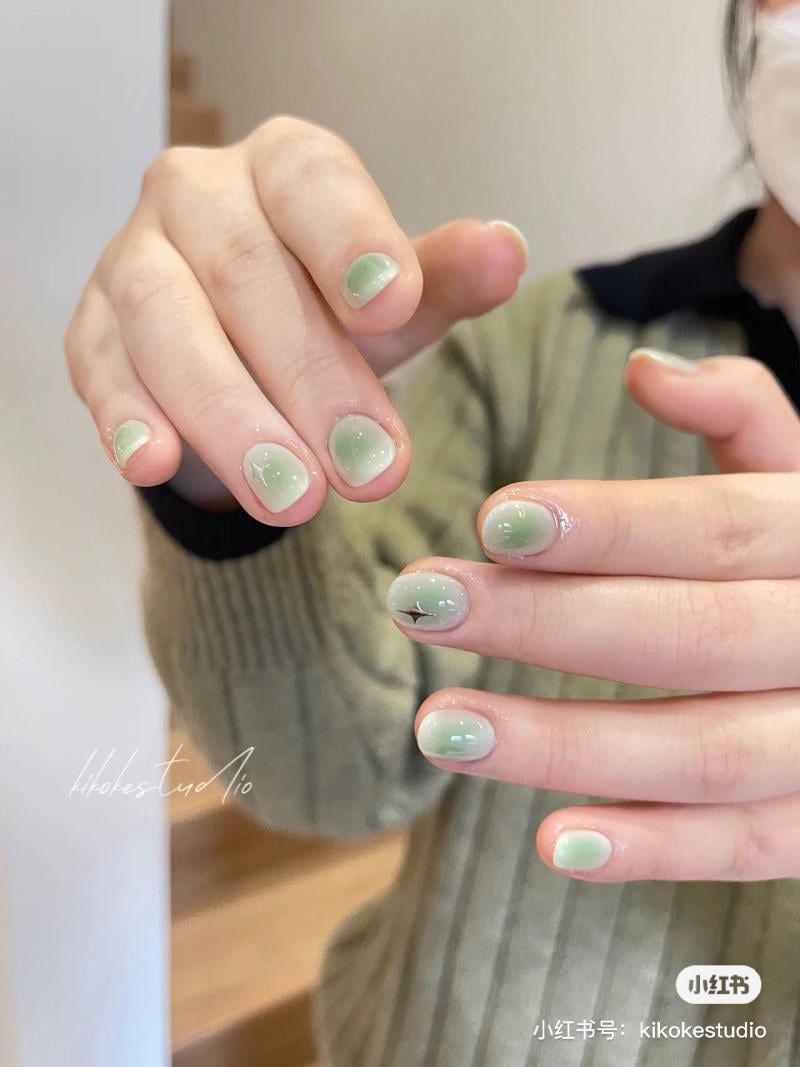 B&agrave;n tay với m&oacute;ng tay sơn m&agrave;u xanh nhạt, c&oacute; họa tiết trang tr&iacute;. Người mặc &aacute;o len m&agrave;u xanh.