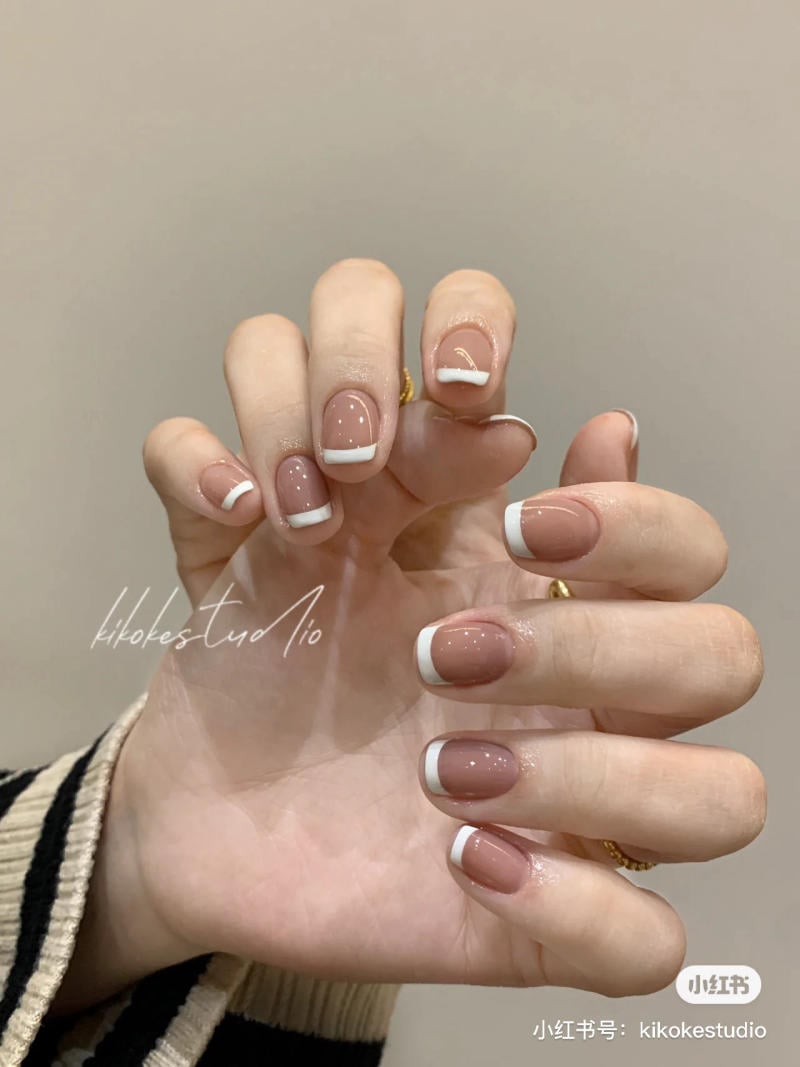 B&agrave;n tay với m&oacute;ng tay sơn m&agrave;u n&acirc;u nhạt, viền trắng, tr&ecirc;n nền m&agrave;u be.