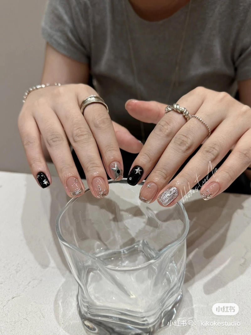 Hai b&agrave;n tay với m&oacute;ng tay được trang tr&iacute; nghệ thuật, cầm một ly thủy tinh trong suốt tr&ecirc;n mặt b&agrave;n.