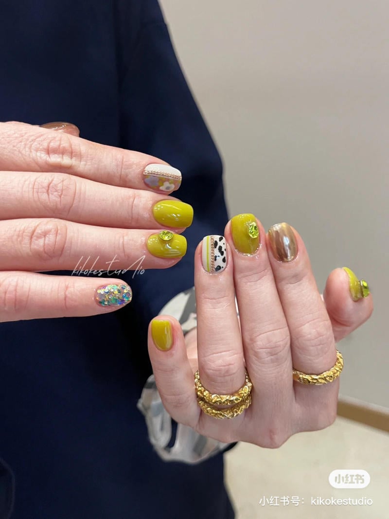 B&agrave;n tay với m&oacute;ng tay được sơn m&agrave;u sắc v&agrave; họa tiết đa dạng, đeo nhiều nhẫn v&agrave;ng, nền &aacute;o tối m&agrave;u.