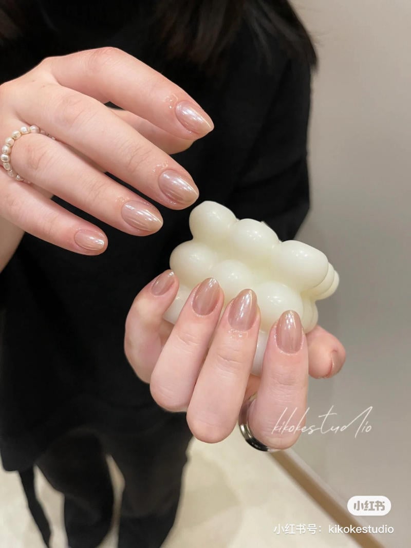 Tay với m&oacute;ng sơn m&agrave;u nude, đang cầm một vật h&igrave;nh đ&aacute;m m&acirc;y m&agrave;u trắng, nền tối m&agrave;u.