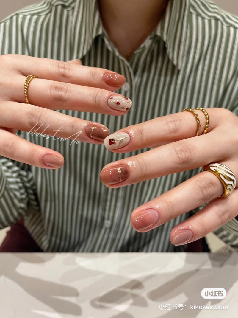 Hai b&agrave;n tay đeo nhẫn, m&oacute;ng tay được sơn v&agrave; trang tr&iacute; họa tiết tinh tế, ph&iacute;a sau l&agrave; &aacute;o sơ mi sọc xanh.