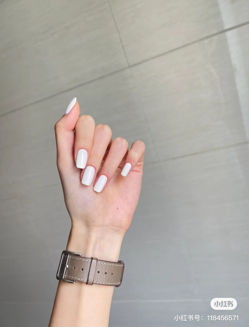 Cánh tay đeo đồng hồ dây da, bàn tay giơ lên với móng tay sơn màu trắng.