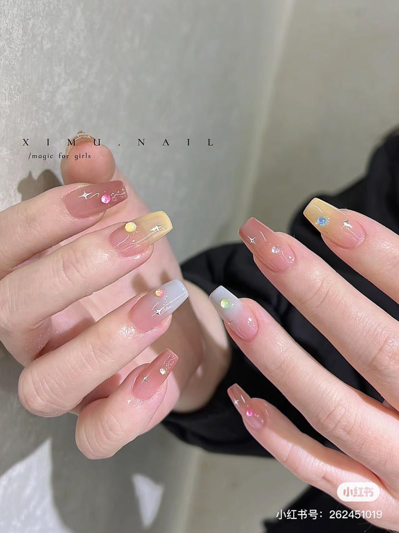Bàn tay với móng tay được sơn màu pastel và trang trí bằng đá quý nhỏ nhiều màu sắc.