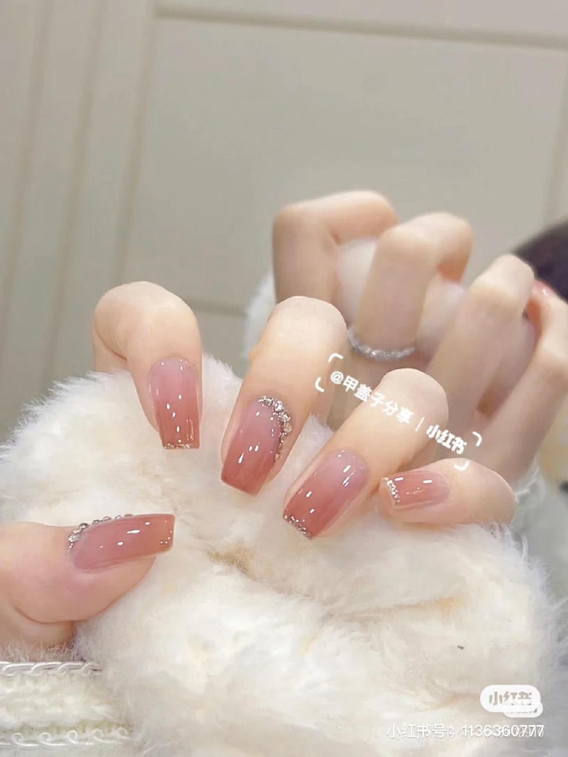 Bàn tay với móng tay sơn màu hồng, đính đá lấp lánh, tựa trên bề mặt lông mềm mại.