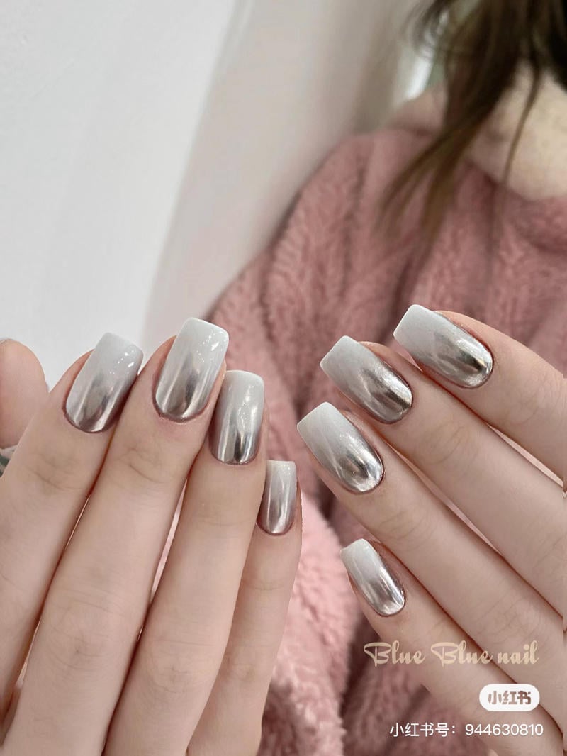 Bàn tay với móng tay được sơn màu trắng và bạc, nền là áo len màu hồng nhạt.