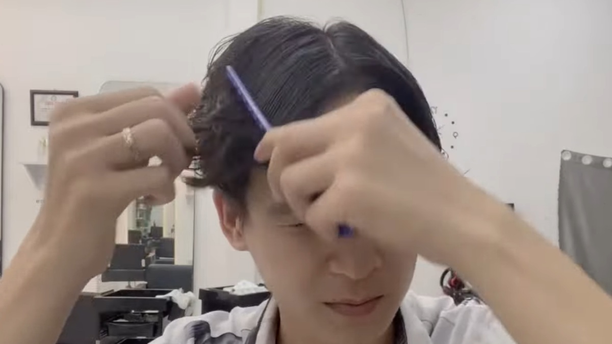 Người đang chải tóc bằng lược màu xanh trong tiệm làm tóc, xung quanh có gương và ghế.