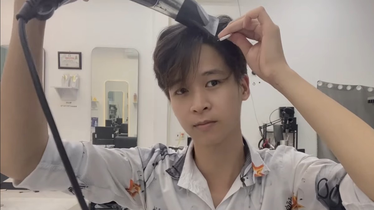 Người đàn ông tự cắt tóc bằng tông đơ trong tiệm, mặc áo sơ mi trắng có họa tiết.