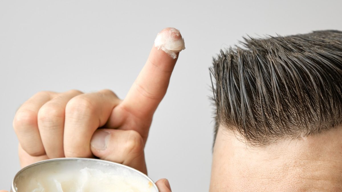 Người đang chấm một ít sáp vuốt tóc từ hộp kim loại và chuẩn bị thoa lên tóc.