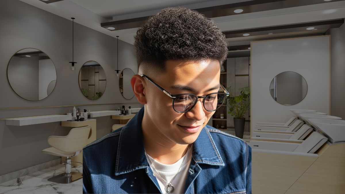 toc-afro-5 Người đeo kính và áo khoác denim đứng trong salon tóc hiện đại với ghế và gương tròn.