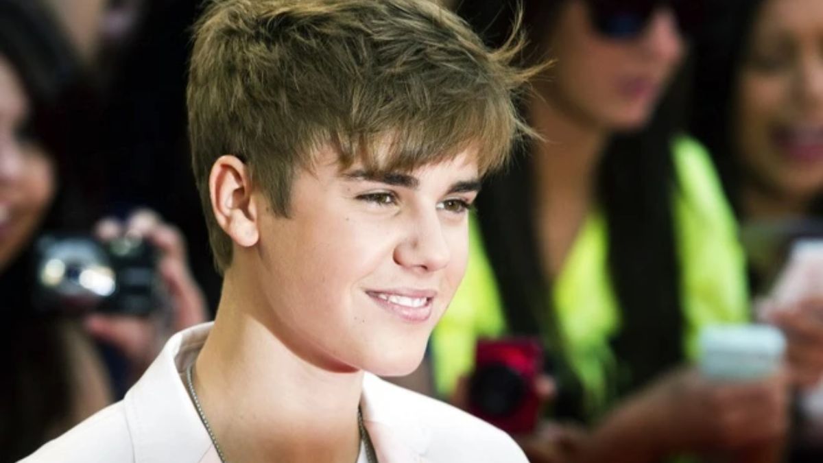 toc-justin-bieber-20 Một người trẻ tuổi đang cười, mặc áo trắng, xung quanh có người chụp ảnh.