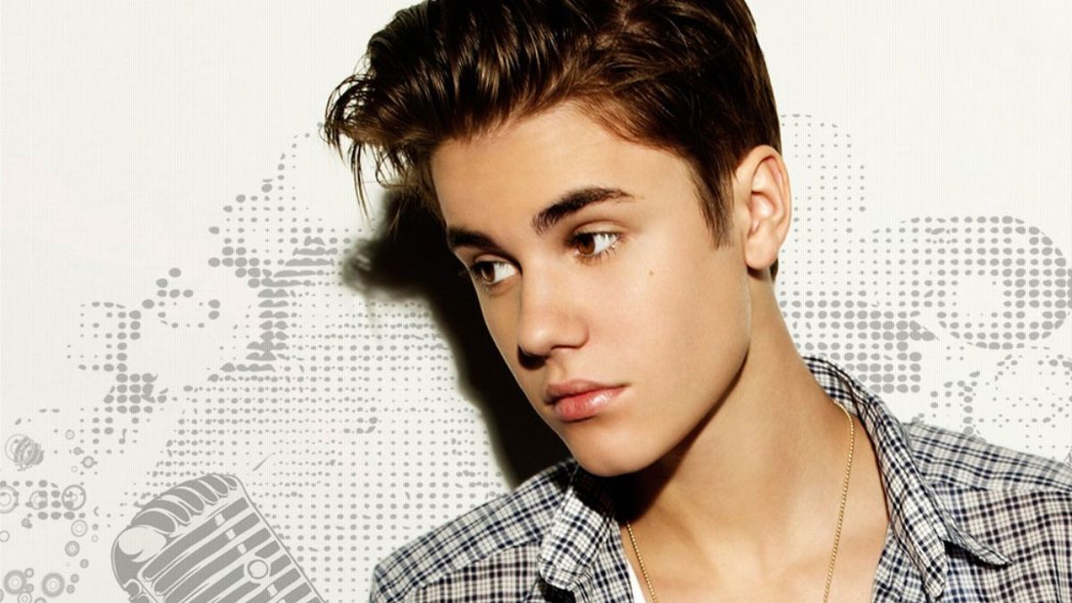 toc-justin-bieber-25 Một người trẻ tuổi với tóc ngắn, mặc áo sơ mi kẻ caro, nhìn nghiêng trong nền trang trí hoa văn.