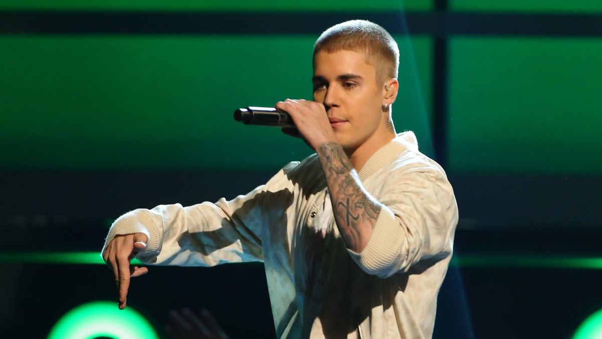 toc-justin-bieber-26 Người đàn ông cầm micro biểu diễn trên sân khấu với ánh sáng xanh phía sau.