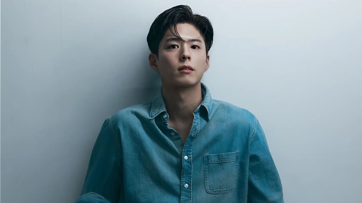 toc-park-bo-gum-1 Người đàn ông mặc áo sơ mi xanh đứng dựa vào tường, nhìn thẳng về phía trước với biểu cảm nghiêm túc.