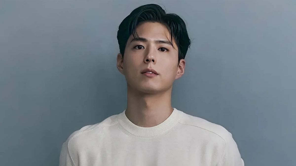 toc-park-bo-gum-2 Người đàn ông mặc áo len trắng, đứng trước nền màu xanh xám, nhìn thẳng vào ống kính.
