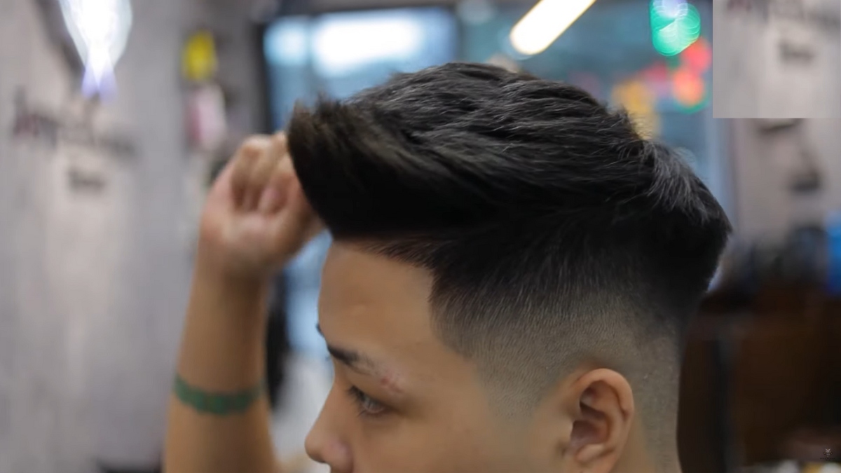 Người đàn ông với kiểu tóc undercut cắt tỉa gọn gàng trong tiệm cắt tóc, nền mờ.