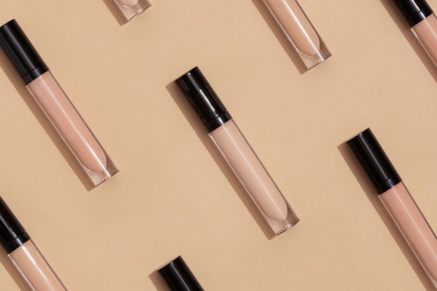 Các ống son lỏng màu nude với nắp đen được xếp chéo trên nền màu be.