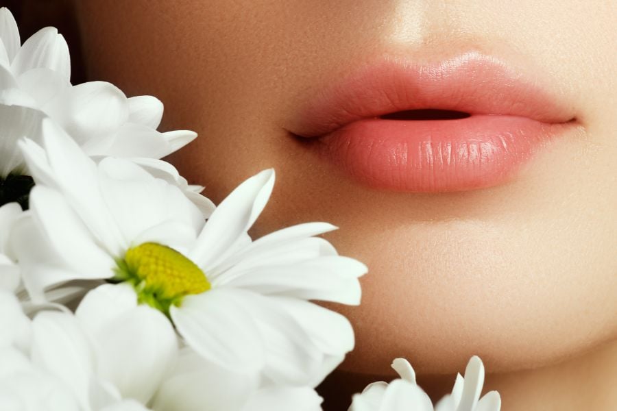 Đôi môi hồng gần những bông hoa cúc trắng, tạo cảm giác nhẹ nhàng và tinh tế.