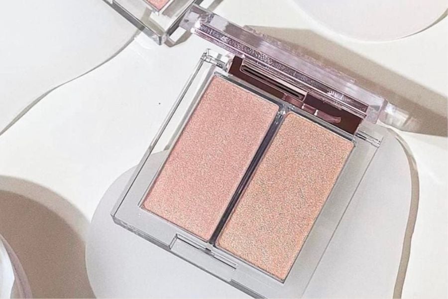 Hộp phấn m&aacute; hồng hai ngăn với t&ocirc;ng m&agrave;u hồng nhạt, đặt tr&ecirc;n bề mặt s&aacute;ng m&agrave;u.