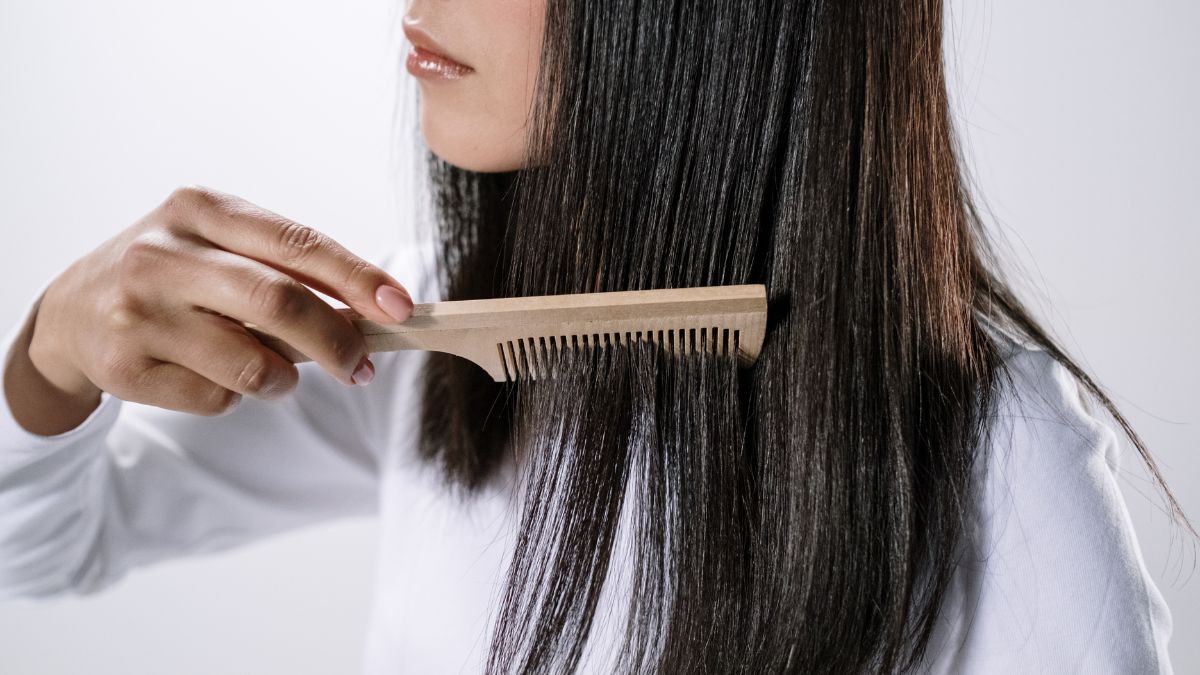 Người đang chải tóc dài và đen bằng lược gỗ, mặc áo trắng, nền trắng.
