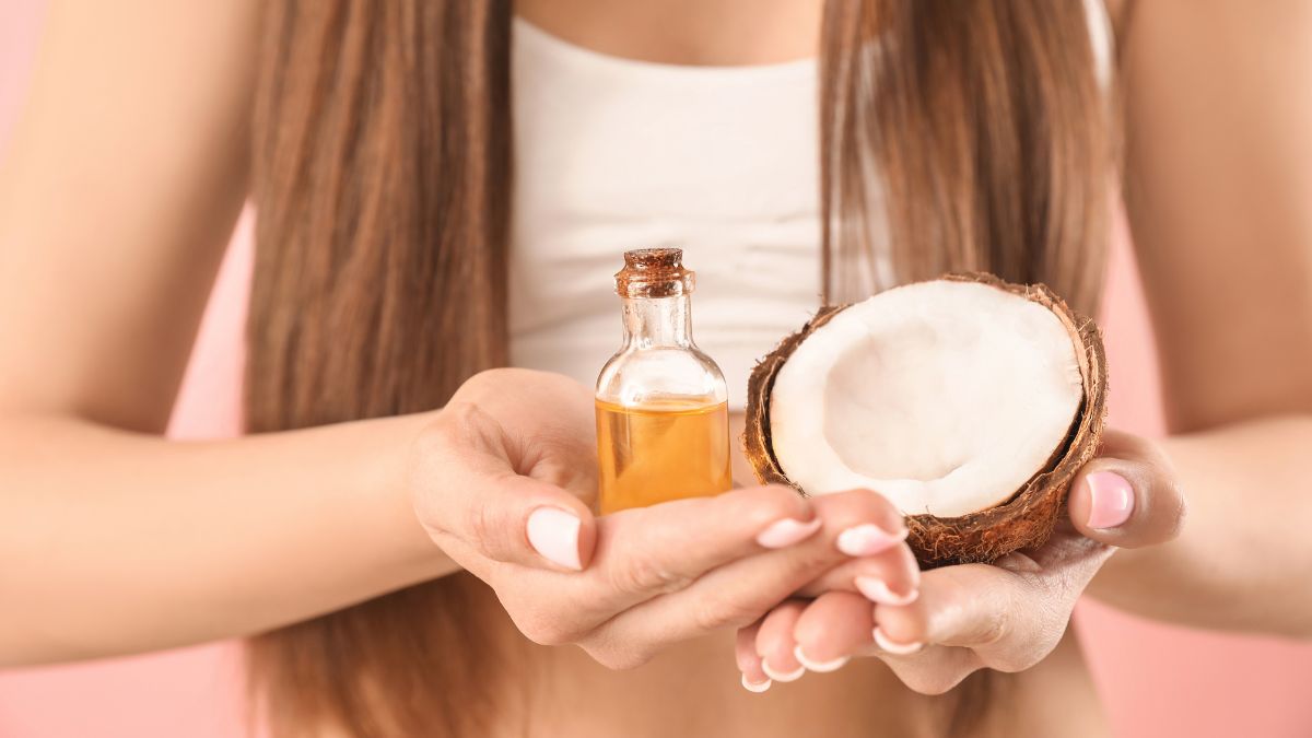 Người cầm nửa quả dừa và chai dầu màu vàng, tóc dài thẳng phía sau.