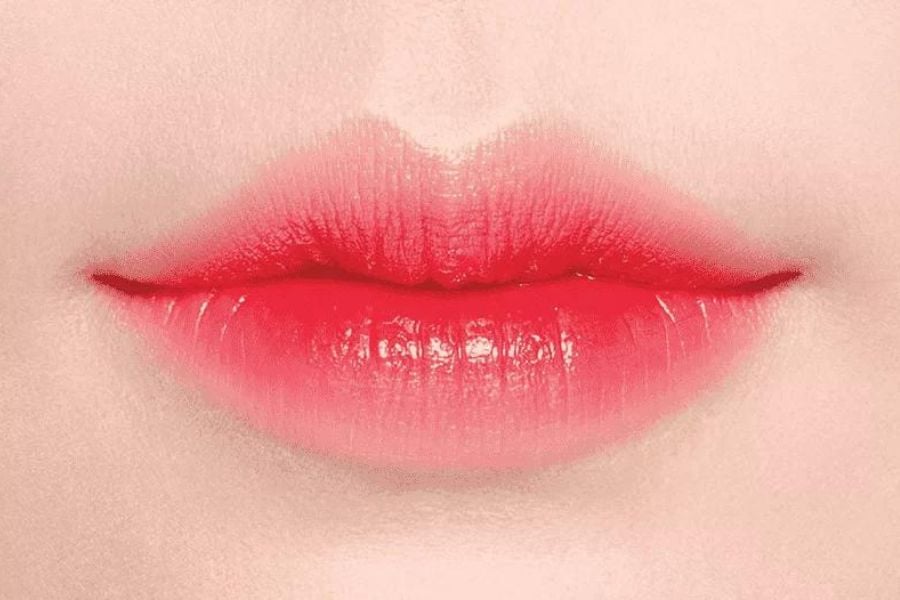 Đôi môi được tô son đỏ đậm, tạo hiệu ứng bóng và mịn màng trên nền da sáng.