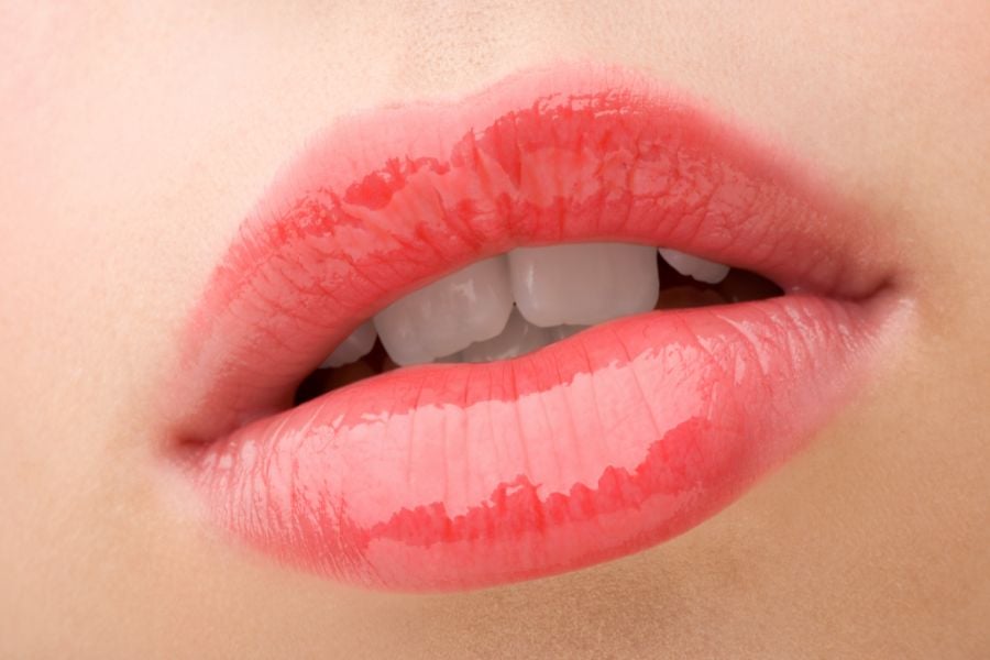 Đôi môi được tô son hồng bóng, răng trắng phía sau.