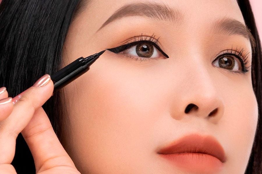 Người đang kẻ mắt bằng bút kẻ mắt màu đen, tập trung vào đôi mắt và đôi môi.