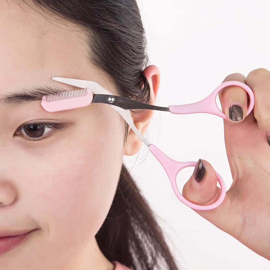 Người sử dụng kéo cắt tỉa lông mày màu hồng có kèm lược để chỉnh sửa dáng lông mày.