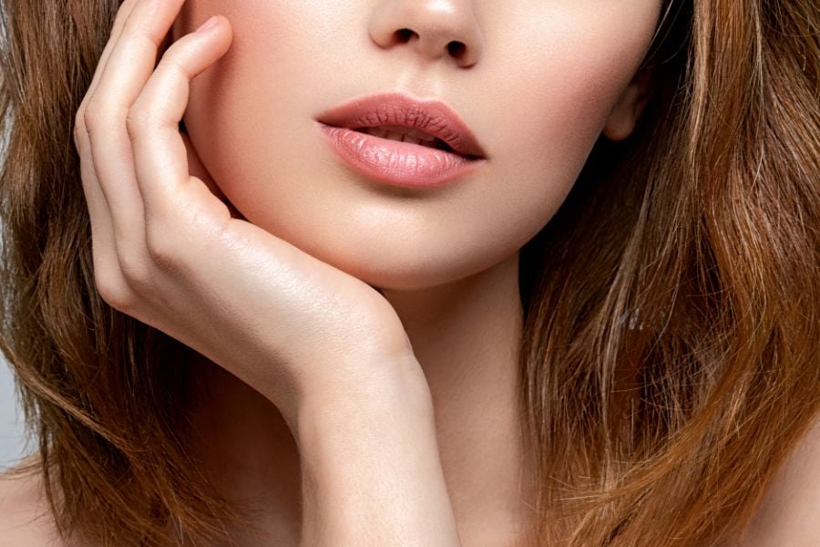 Cận cảnh khuôn mặt người với đôi môi và tay chạm nhẹ lên má, tóc nâu xõa xuống vai.