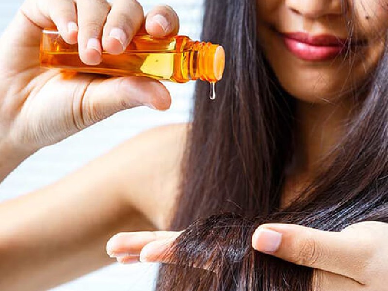 Người đang nhỏ dầu dưỡng từ chai màu cam lên tóc, tập trung vào chăm sóc tóc.