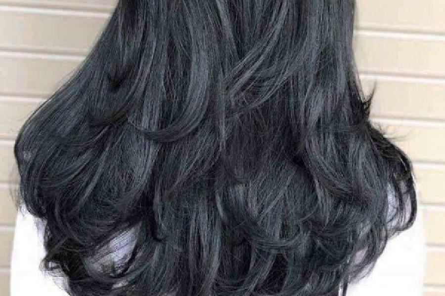 20 Kiểu Tóc Đen Đẹp Giúp Nàng Trẻ Trung và Hack Tuổi Hiệu Quả 7 Mái tóc đen dài và dày, uốn lượn sóng nhẹ, được chụp từ phía sau trên nền tường sáng.