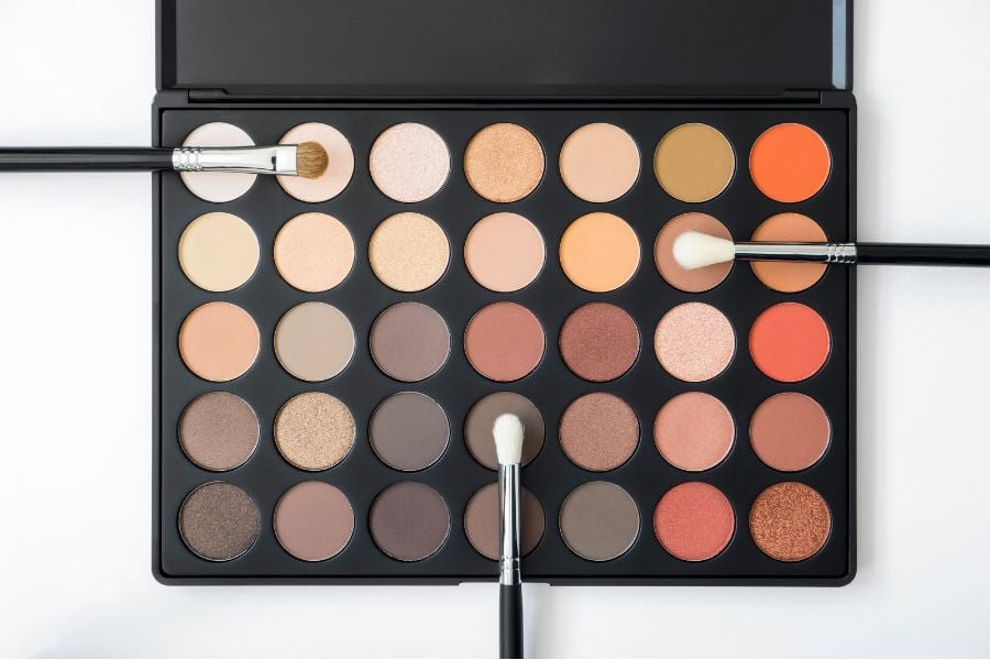 bang-mau-mat_3a9eb925ea354e248a3cf9560fba295e Bảng phấn mắt với nhiều màu sắc khác nhau, có ba cọ trang điểm đặt trên bề mặt.