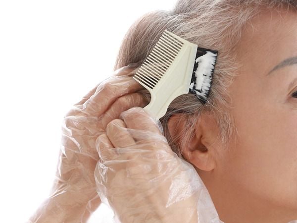 Một người đang tự nhuộm tóc, sử dụng lược chải thuốc lên tóc bạc, tay đeo găng tay nhựa.