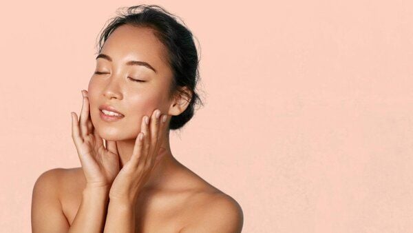 Người phụ nữ thư giãn, nhắm mắt, chạm vào mặt trên nền màu hồng.