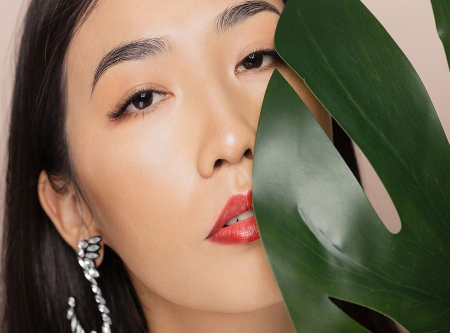 Người phụ nữ với đ&ocirc;i m&ocirc;i đỏ v&agrave; b&ocirc;ng tai lớn, che một phần khu&ocirc;n mặt bằng l&aacute; xanh.