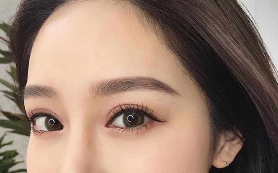 Cận cảnh phần trên khuôn mặt với đôi mắt trang điểm kỹ lưỡng và lông mày đậm, tóc nâu.