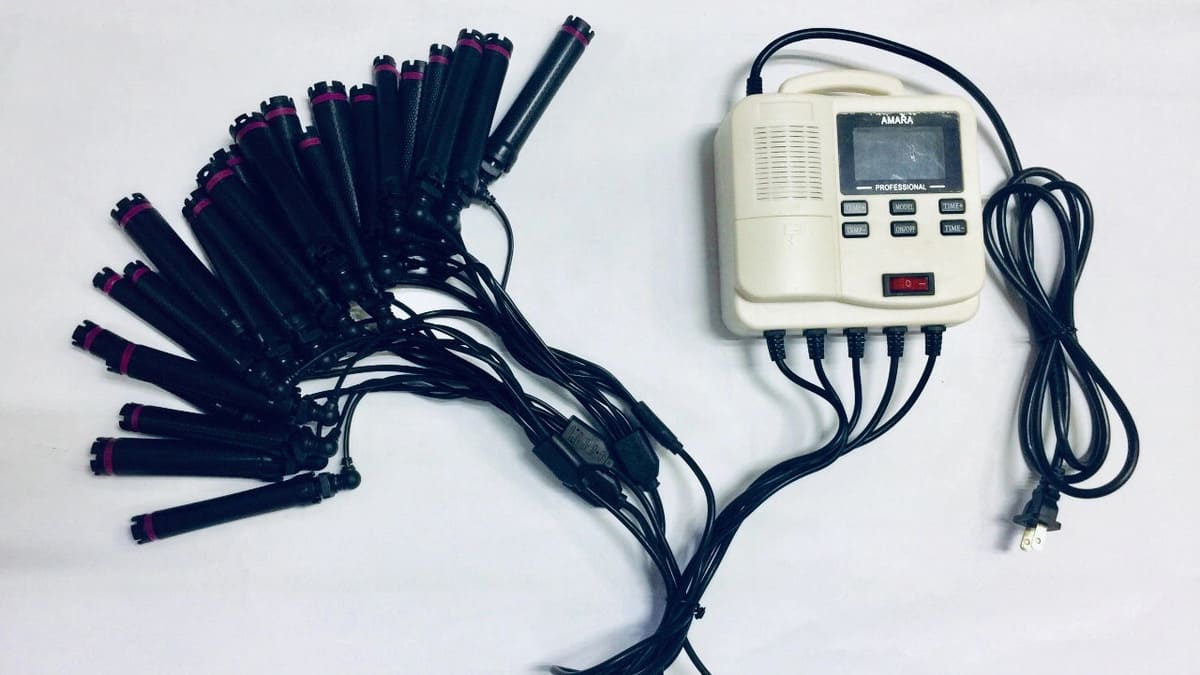 Máy uốn tóc tự động với nhiều lô cuốn màu đen có viền hồng, kết nối qua dây điện với bảng điều khiển.