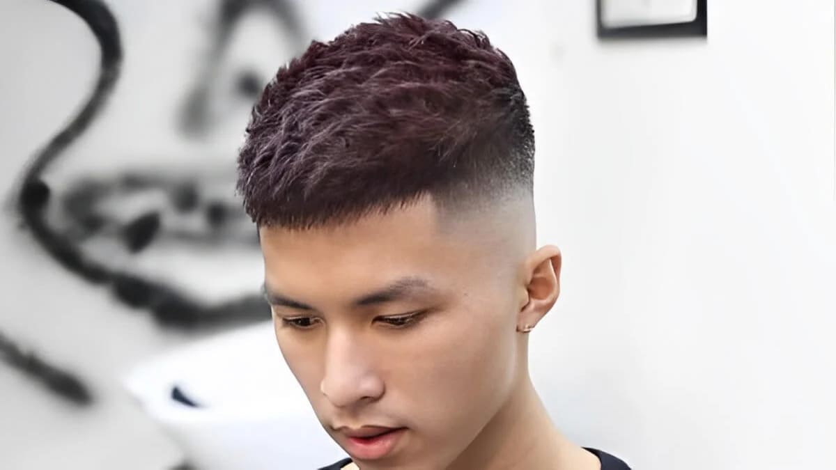 Người đàn ông với kiểu tóc ngắn gọn gàng, phần trên được cắt tỉa và nhuộm màu nâu, trong không gian hiện đại.