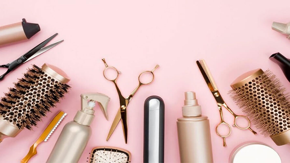 cach-cat-toc-layer-tai-nha-1 Dụng cụ cắt tóc và chăm sóc tóc trên nền màu hồng, bao gồm kéo, lược và chai xịt.