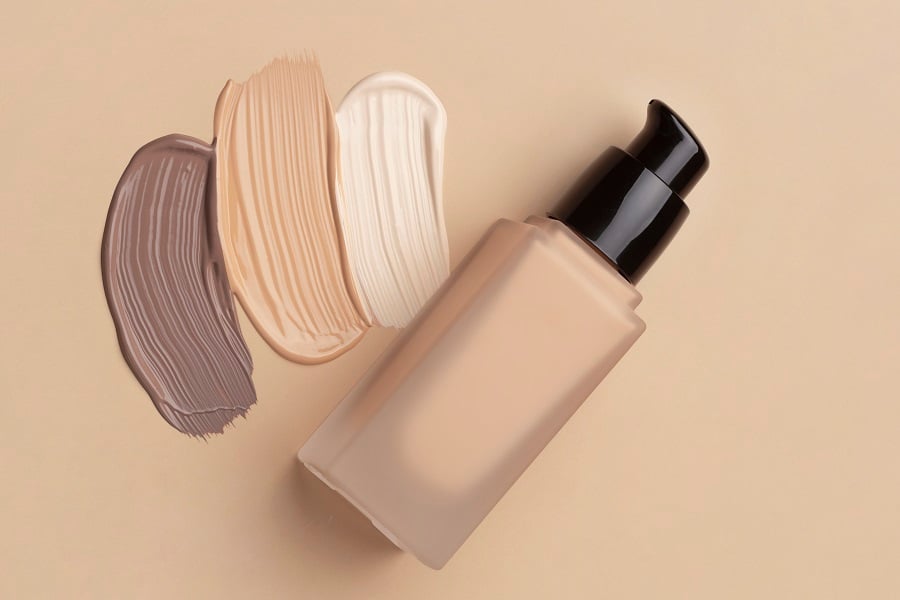 cach-che-khuyet-diem-tren-mat-1_3f25455f217f4321bf40b174122153cd Chai kem nền với nắp đen, bên cạnh là các vệt màu kem trang điểm khác nhau trên nền be.