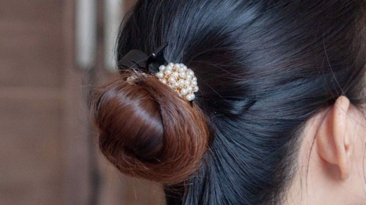Mái tóc búi gọn gàng được trang trí với kẹp tóc đính hạt ngọc trai, mang lại vẻ thanh lịch và tinh tế.