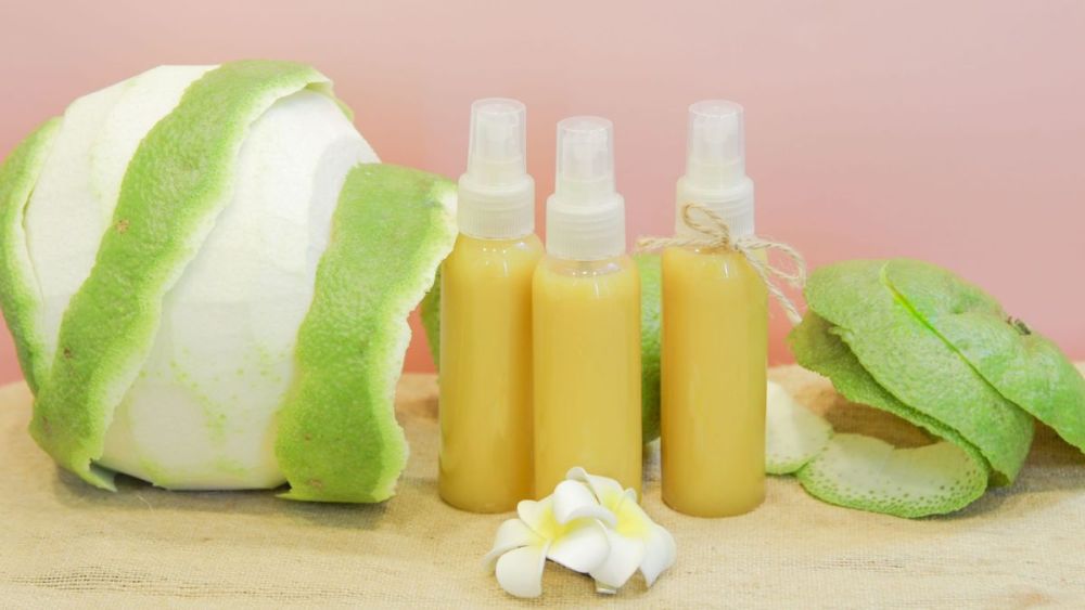 cach-lam-toc-muot-4 Ba chai xịt màu vàng cam đặt cạnh vỏ bưởi xanh và hoa trắng trên nền hồng nhạt.